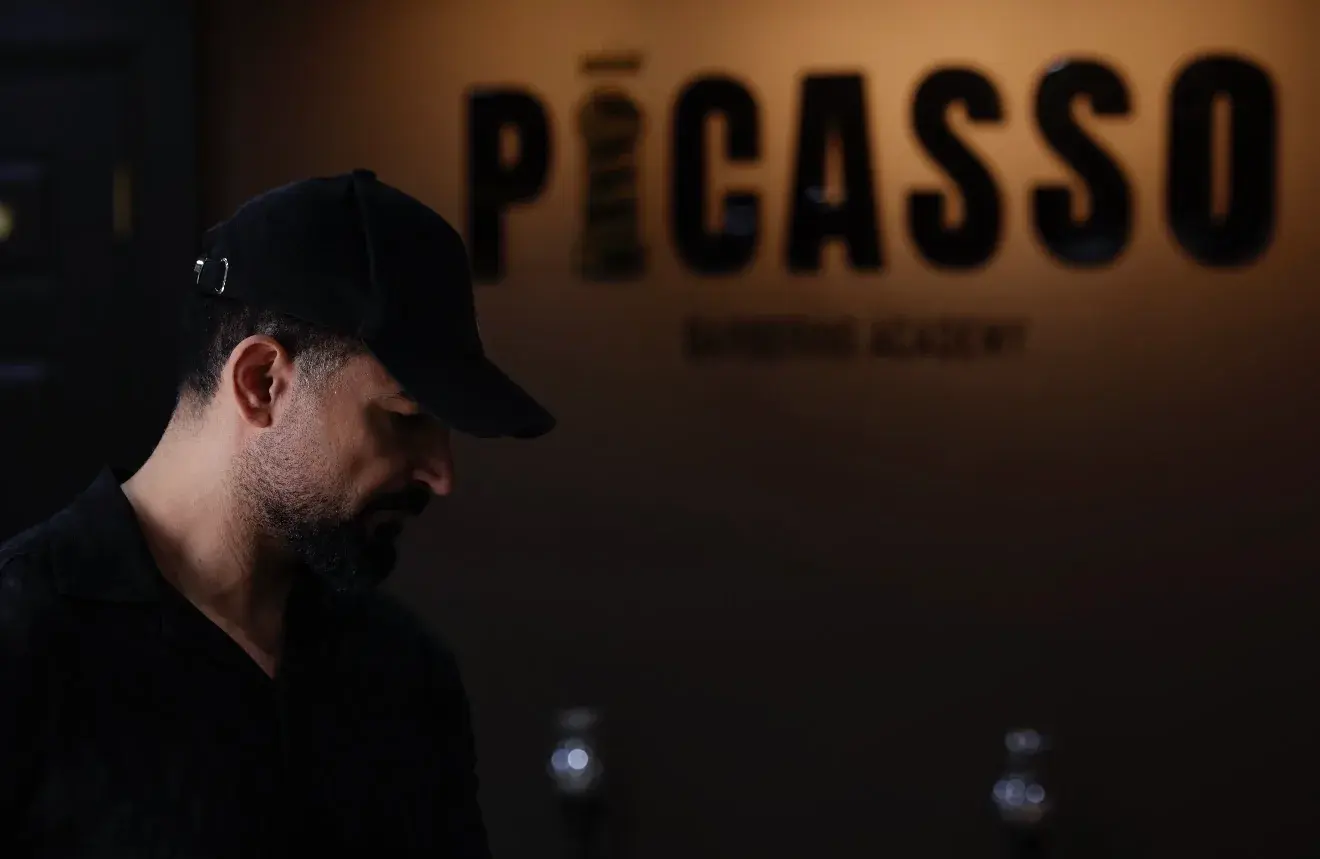 Barber at Picasso Academy with the academy sign behind him